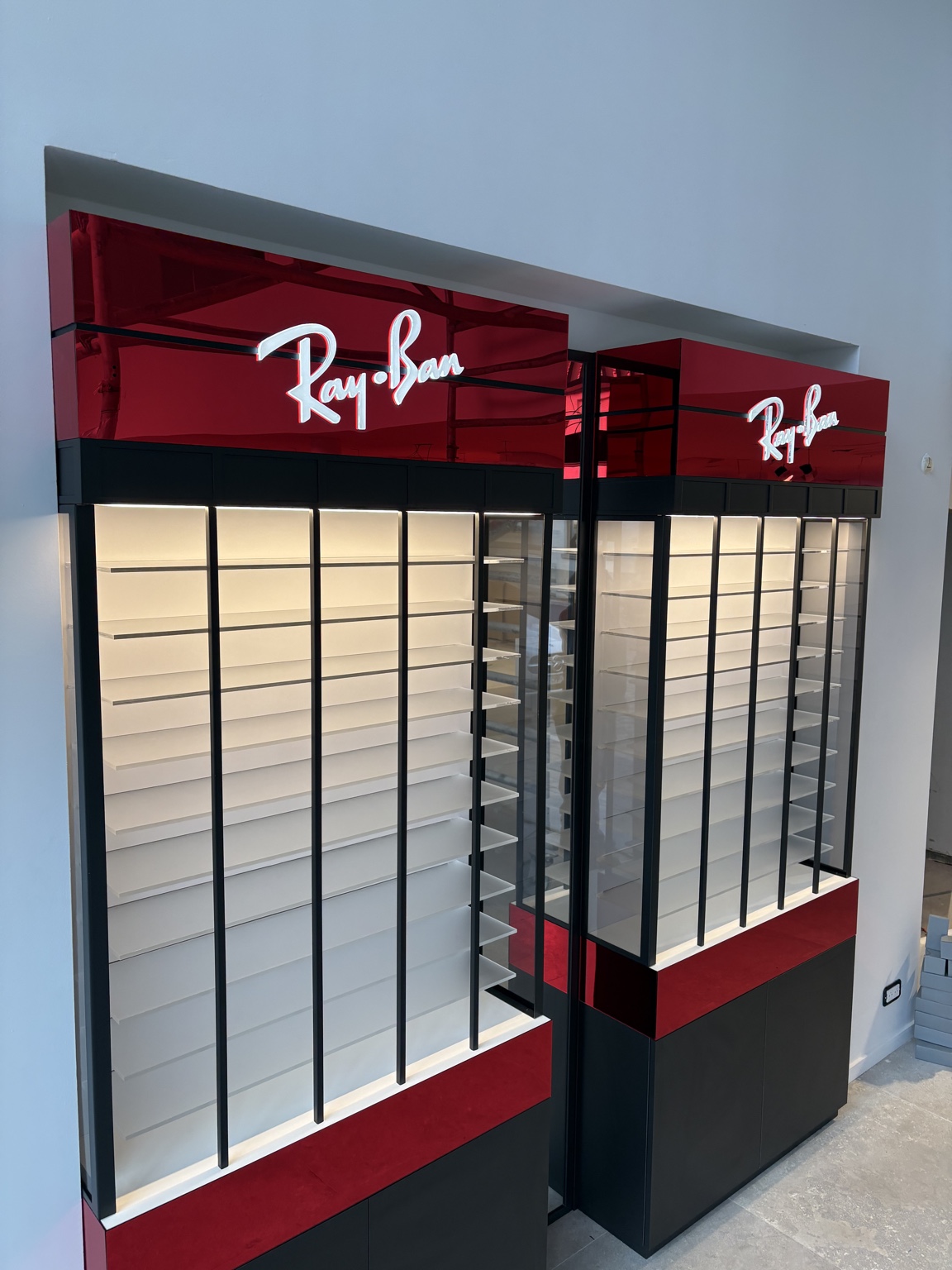 Deux vitrines murales Ray-Ban avec bandeaux rouge miroir, montants noirs et éclairage intégré