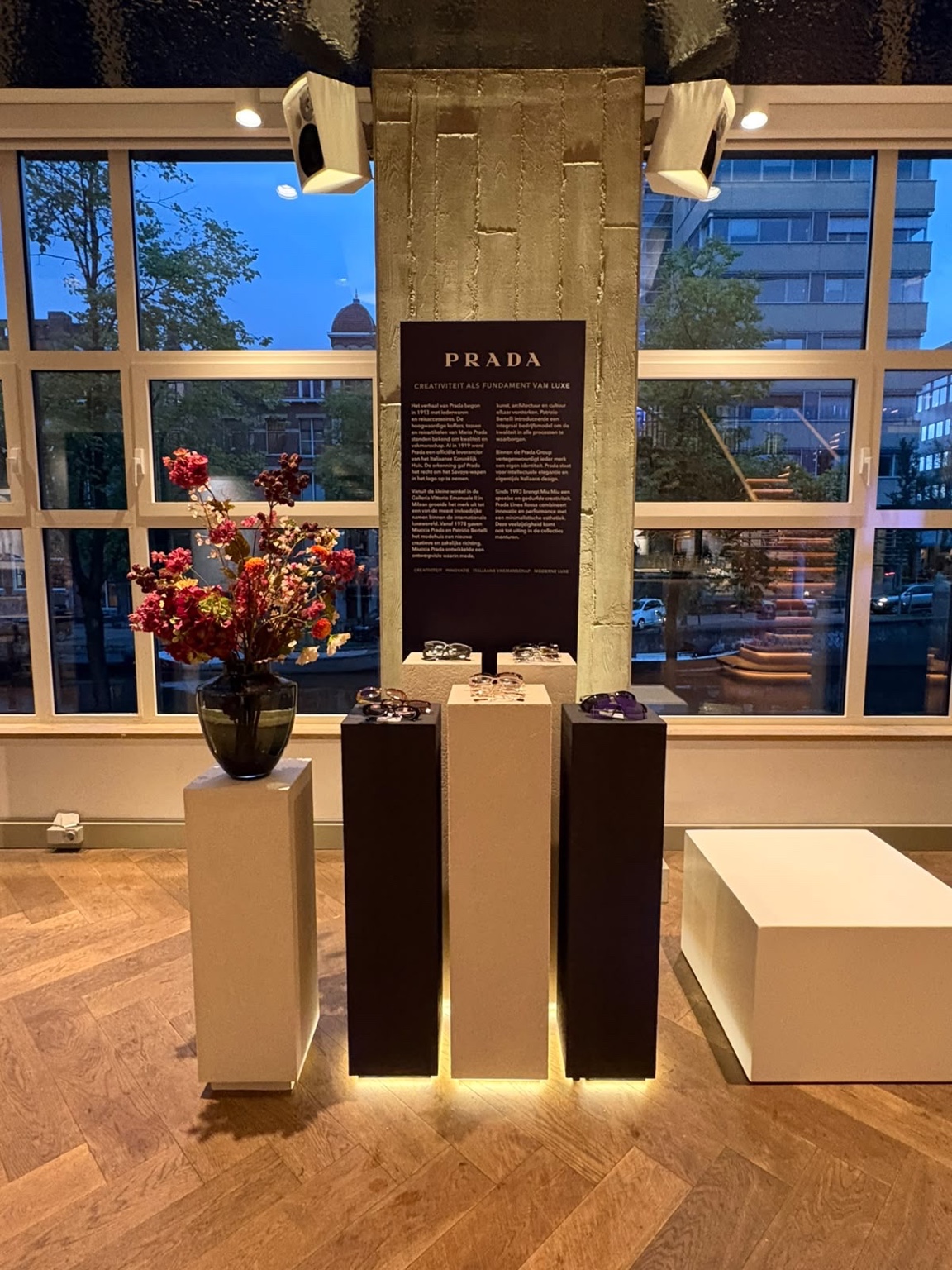 Stèles claires et foncées avec éclairage en pied, présentant des lunettes devant un panneau Prada